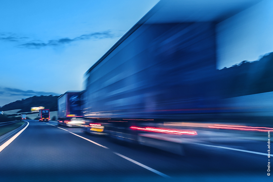 Das Bild zeigt mehrere LKW auf der linken Spur einer Autobahn. Sie sind verwischt dargestellt, was ihre hohe Geschwindigkeit ver